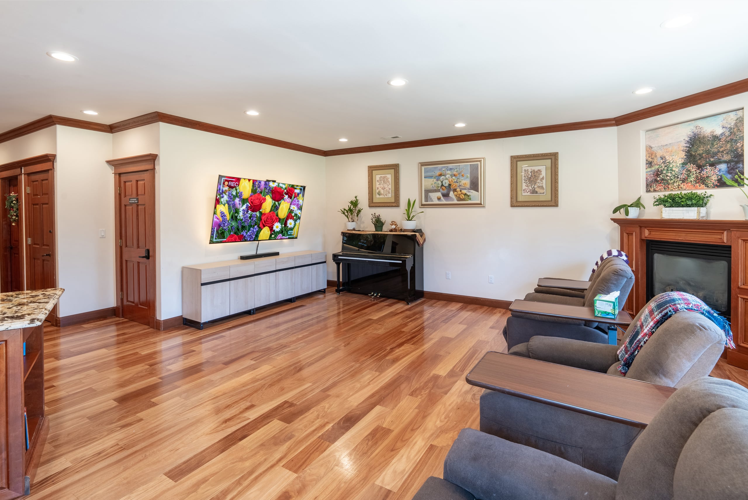 The main living room with a wall-mounted television, an upright piano, recliners and a gas fireplace.